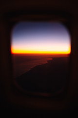 Beautiful scenic view through the aircraft window at sunset or sunrise time. Window view from passenger seat  airplane. Flying above the clouds. Panorama high above city. Vacation and travel concept.
