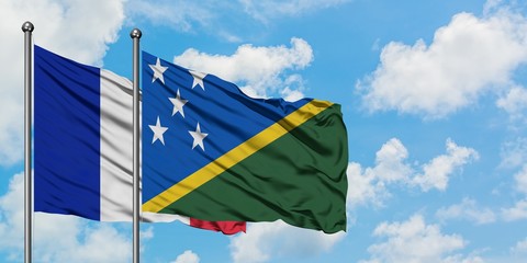 France and Solomon Islands flag waving in the wind against white cloudy blue sky together....