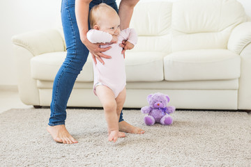 First steps of baby toddler learning to walk in white sunny living room. Footwear for child.