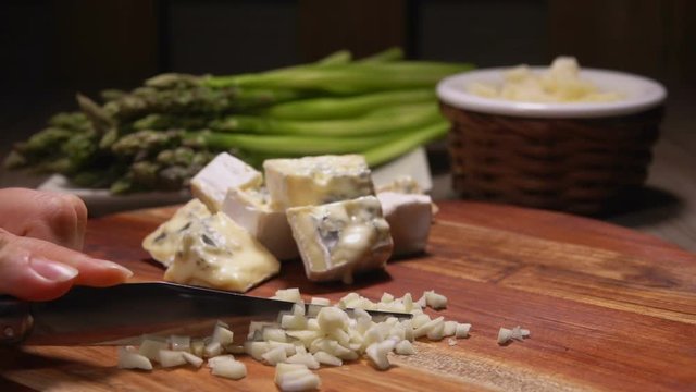 Hands chop garlic into small cubes on a background of cheese and asparagus. Cheese Sauce Ingredients
