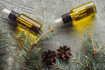 top view of bottles with natural oil near fir branches and dry cones on grey stone surface