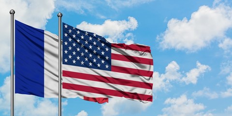 Obraz premium France and United States flag waving in the wind against white cloudy blue sky together. Diplomacy concept, international relations.