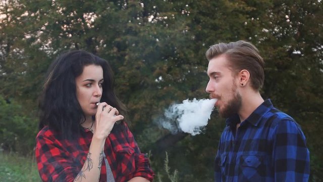 young beautiful couple vaping e-cigarette in the park. Slow motion