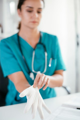 Young female doctor in medical office. Close up of female doctor putting gloves on.