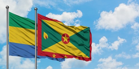 Gabon and Grenada flag waving in the wind against white cloudy blue sky together. Diplomacy...