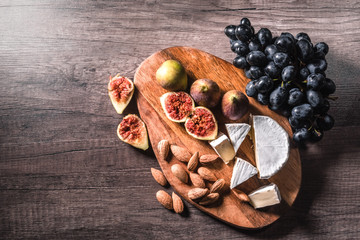 Cheese plate served with grapes, figs and nuts on a wooden background.