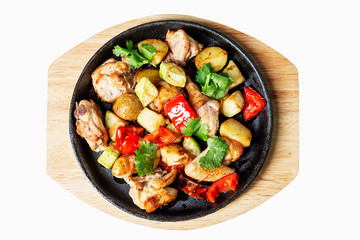 Roasted vegetables on a cast-iron pan served on a wooden board. Top view. Isolated over white...
