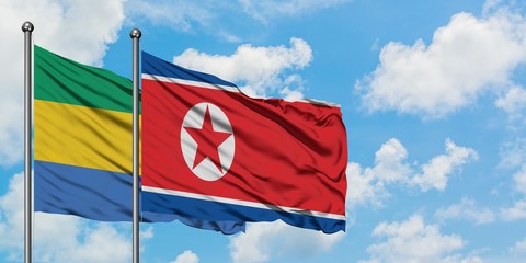 Gabon and North Korea flag waving in the wind against white cloudy blue sky together. Diplomacy...
