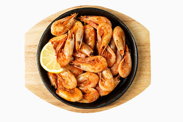 Appetizing fried shrimp with lemon in a serving cast-iron skillet. Top view. Isolated over white background.