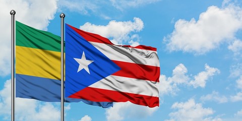 Gabon and Puerto Rico flag waving in the wind against white cloudy blue sky together. Diplomacy...