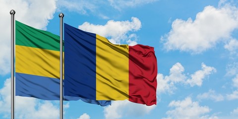 Gabon and Romania flag waving in the wind against white cloudy blue sky together. Diplomacy...