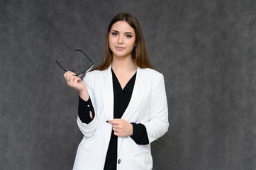 Close-up portrait of a young pretty girl secretary with long black hair in a business suit, on a gray background. Standing right in front of the camera in different poses with emotions.