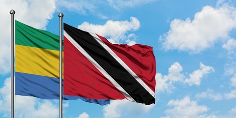 Gabon and Trinidad And Tobago flag waving in the wind against white cloudy blue sky together....