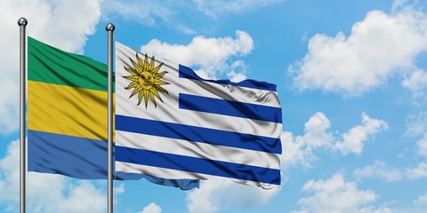 Gabon and Uruguay flag waving in the wind against white cloudy blue sky together. Diplomacy...