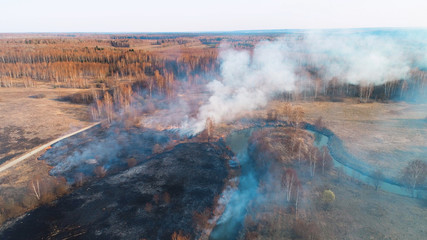 Flying over a fire in the forest. Black burned field, there is a strong thick smoke. A small river blocks the path of fire.