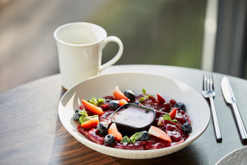 traditional Ukrainian varenyky with berries served in white plate with sauce near cutlery and cup on wooden table in restaurant