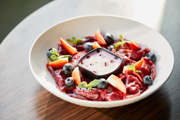close up view of traditional Ukrainian varenyky with berries served in white plate with sauce on wooden table in sunlight