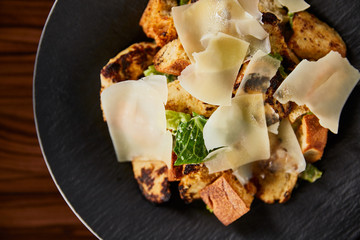 tasty Caesar salad with Parmesan slices served on plate on wooden table
