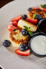 close up view of traditional Ukrainian dish syrniki with strawberry, blueberry served with jam and sour cream