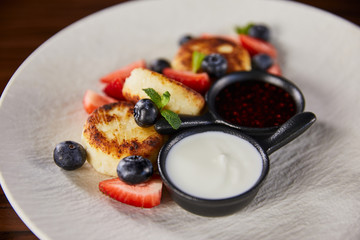 close up view of traditional Ukrainian dish syrniki with strawberry, blueberry served with jam and sour cream