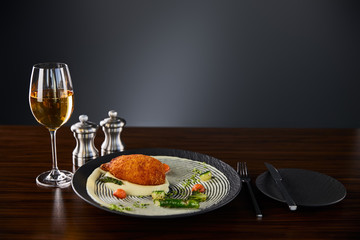 delicious chicken kiev and mashed potato served on plate near cutlery and white wine on black background