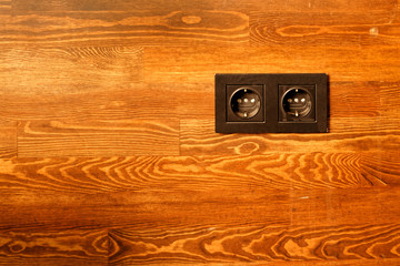 Black power outlet on brown varnished wood wall background
