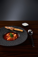 traditional ukrainian borscht garnished with parsley in black plate served with sour cream near spoon at wooden table