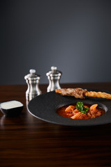 traditional ukrainian borscht garnished with parsley in black plate served with sour cream and seasoning at wooden table