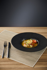delicious restaurant soup with shrimps in black plate served on napkin with cutlery