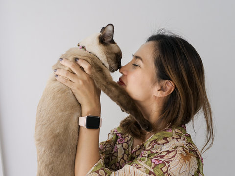 Asian woman holding  and kissing her cat with window light at home.