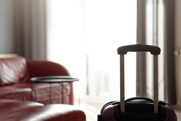 A suitcase standing by the window in the living room near a large leather red sofa and an empty...