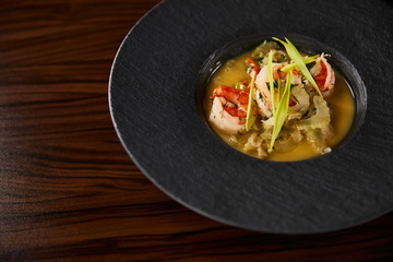 close up view of delicious restaurant soup with shrimps in black plate on wooden table