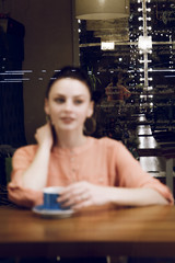 Fototapeta na wymiar portrait of young woman drinking coffee at table in cafe through the window