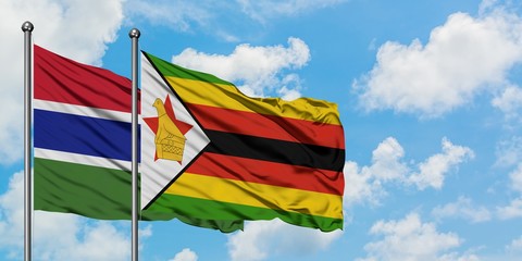 Gambia and Zimbabwe flag waving in the wind against white cloudy blue sky together. Diplomacy...