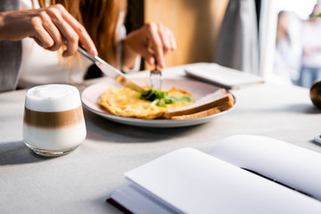 cropped view of woman eating breakfast with coffee in cafe with empty notepad