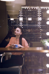 Fototapeta na wymiar portrait of young woman drinking coffee at table in cafe through the window