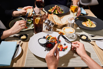 cropped view of woman eating delicious syrniki during dinner with friends in restaurant