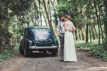 Happy beautiful bride and groom hugging in the woods near the car.