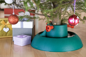 Plastic Christmas tree stand with poured water surrounded by gift boxes stands at home in New Year eve on the floor in city flat