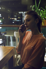 portrait of young woman drinking coffee at table in cafe through the window
