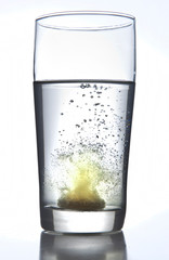 Effervescent or carbon tablet dissolving in water in a high ball tumbler glass on a white background.