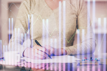 Hand taking notes in notepad. Forex chart holograms in front. Concept of research. Double exposure
