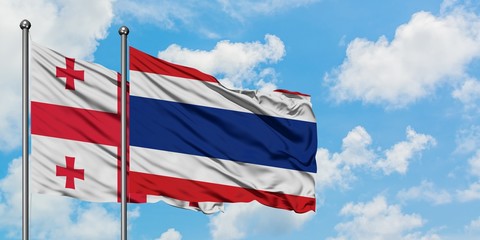 Georgia and Thailand flag waving in the wind against white cloudy blue sky together. Diplomacy...