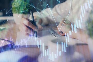 Financial forex graph displayed on hands taking notes background. Concept of research. Multi...