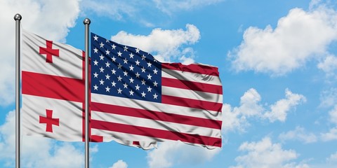 Georgia and United States flag waving in the wind against white cloudy blue sky together. Diplomacy concept, international relations.