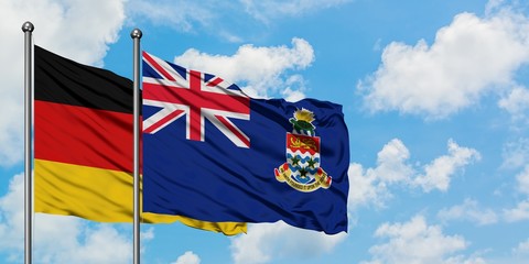 Germany and Cayman Islands flag waving in the wind against white cloudy blue sky together....