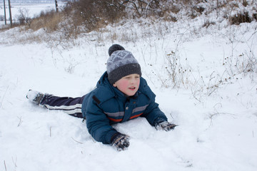 Fototapeta na wymiar boy resting in the snow, happy boy lies in the snow in winter with a rosy face