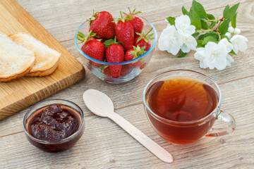 Glass cup of tea, bread, strawberries with white jasmine flowers