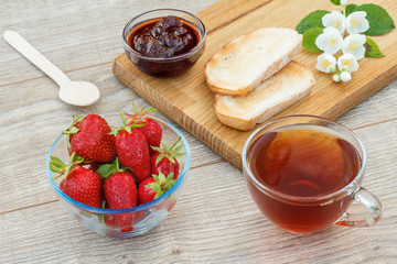 Glass cup of tea, bread, strawberries with white jasmine flowers