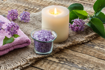 Fototapeta na wymiar Towel, sea salt, candle and lilac flowers on wooden background.